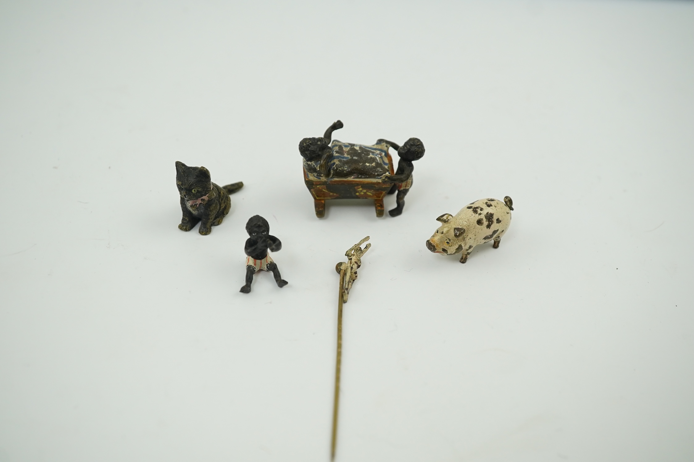 Four novelty miniature cold painted bronzes; black boy with cradle, black baby, cat and pig and a similar articulated arm skeleton stickpin,7cm long. Condition - some chipping to paint